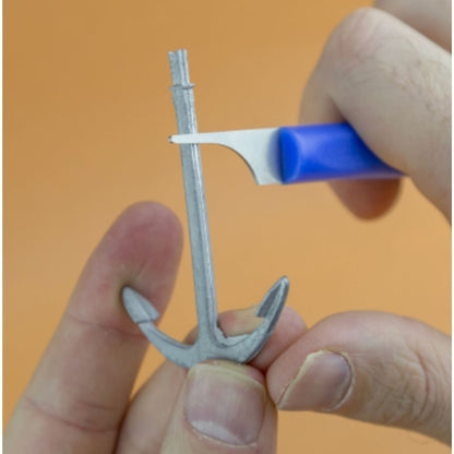 Small plastic anchor held by a hand with a blue Mold and sprue cleaning tool against an orange background